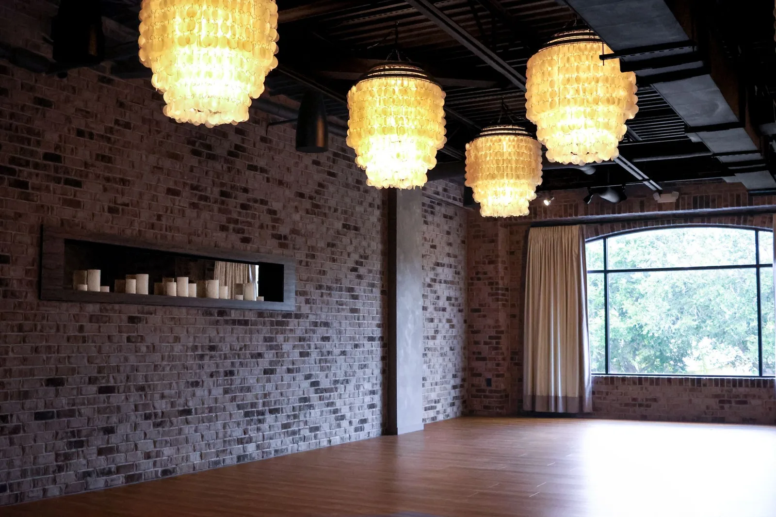 The empty Red Skies studio with capiz chandeliers, brick walls and a big arched window